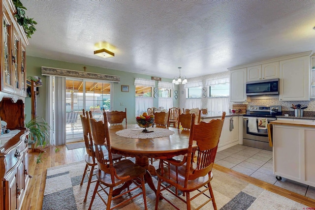 dining room featuring light wood-type flooring, a textured ceiling, a wealth of natural light, and a chandelier