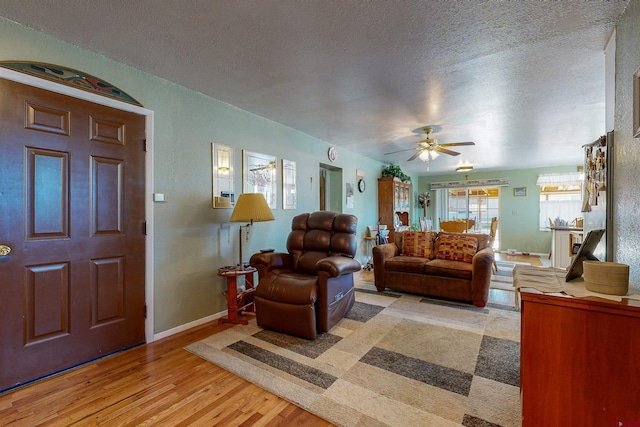 living room featuring ceiling fan, light hardwood / wood-style floors, and a textured ceiling