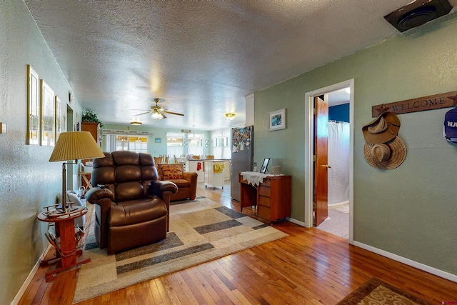 living room featuring ceiling fan, light hardwood / wood-style flooring, and a textured ceiling