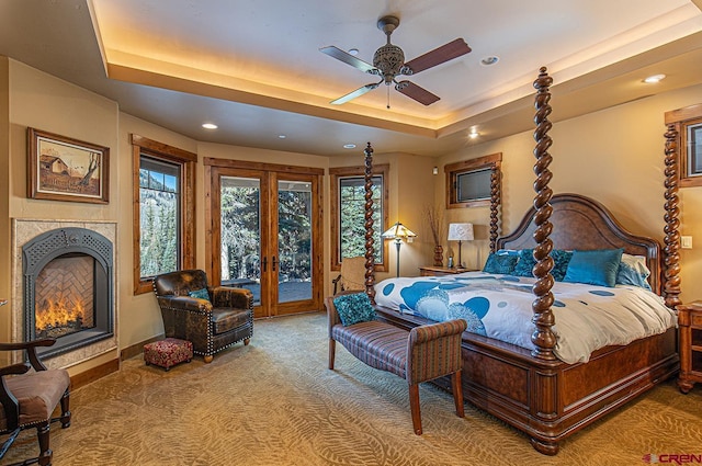 carpeted bedroom featuring access to exterior, a tray ceiling, ceiling fan, and a fireplace