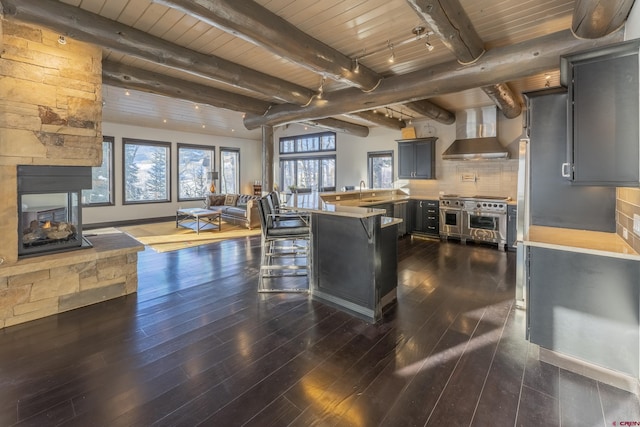 kitchen featuring decorative backsplash, a kitchen breakfast bar, wall chimney range hood, range with two ovens, and a fireplace