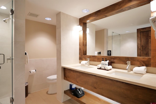 bathroom with vanity, a shower with door, tile patterned floors, toilet, and tile walls