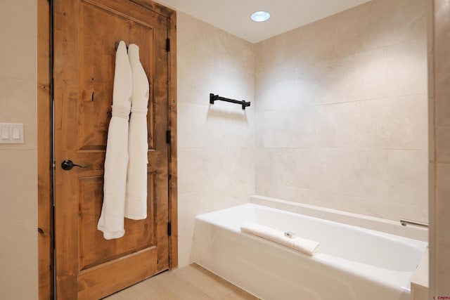 bathroom with tile patterned flooring, tile walls, and a tub