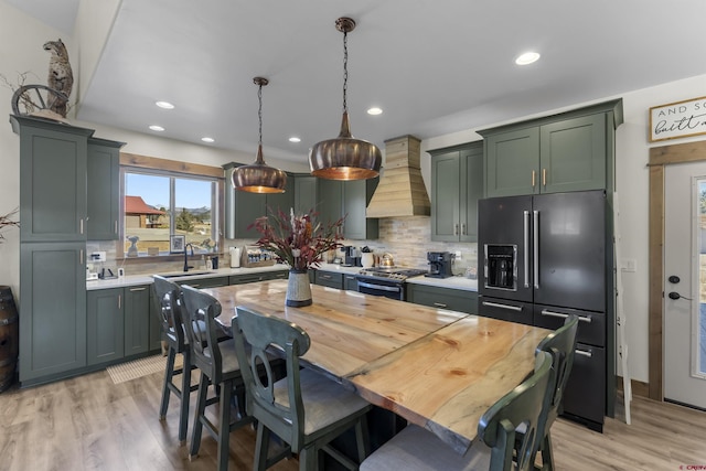 kitchen featuring stainless steel range with gas cooktop, premium range hood, backsplash, pendant lighting, and high quality fridge