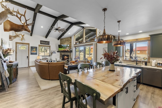 kitchen with ceiling fan, sink, a stone fireplace, lofted ceiling with beams, and stainless steel dishwasher