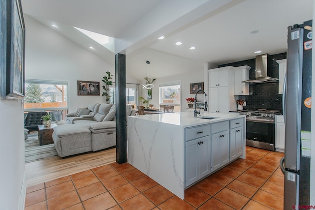 kitchen with sink, stainless steel appliances, wall chimney range hood, an island with sink, and vaulted ceiling