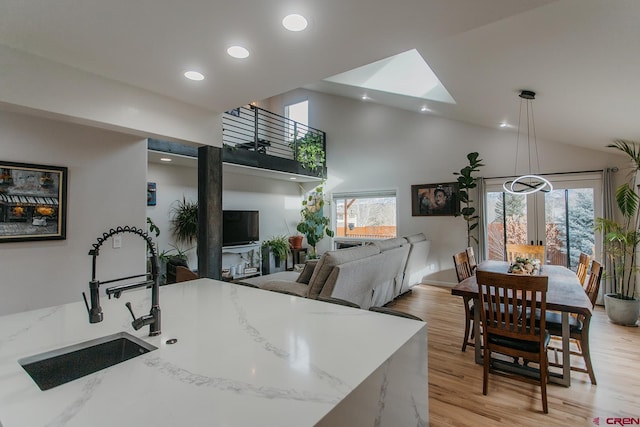 kitchen with high vaulted ceiling, sink, decorative light fixtures, light hardwood / wood-style floors, and light stone counters