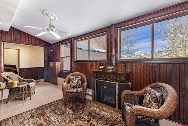 living area featuring ceiling fan, wooden walls, light tile patterned floors, and lofted ceiling