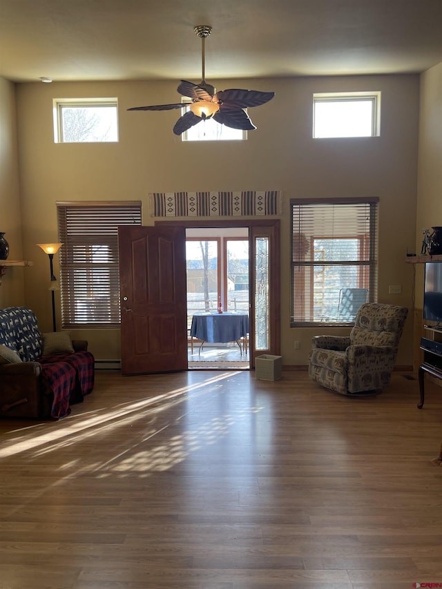 living room with hardwood / wood-style floors, ceiling fan, a towering ceiling, and a baseboard radiator