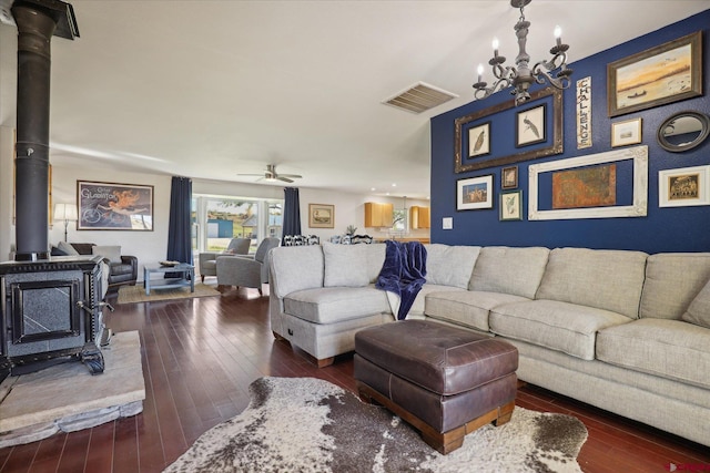 living room featuring ceiling fan with notable chandelier, dark hardwood / wood-style floors, and a wood stove