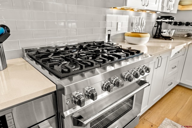 interior details with white cabinets, decorative backsplash, high end stove, and light hardwood / wood-style flooring