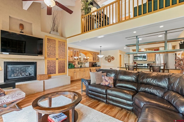 living room with ceiling fan with notable chandelier, a towering ceiling, and light hardwood / wood-style flooring