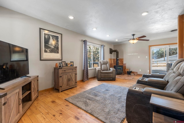 living room with light wood-type flooring, a wood stove, and ceiling fan