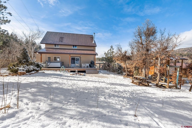 snow covered property with a wooden deck and a hot tub