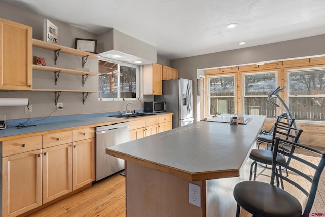 kitchen featuring light brown cabinets, a center island, sink, appliances with stainless steel finishes, and a kitchen bar