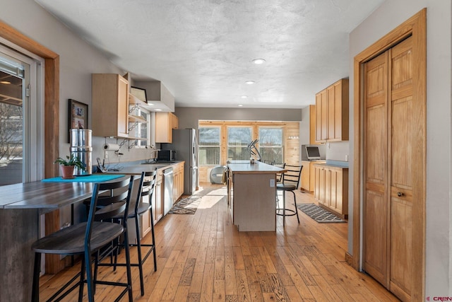 kitchen with appliances with stainless steel finishes, a breakfast bar, a textured ceiling, light hardwood / wood-style flooring, and a center island