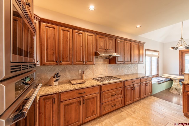 kitchen with tasteful backsplash, light stone counters, stainless steel appliances, decorative light fixtures, and light hardwood / wood-style floors