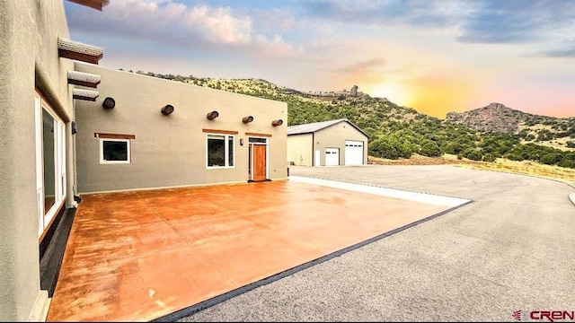 patio terrace at dusk with a mountain view, an outbuilding, and a garage