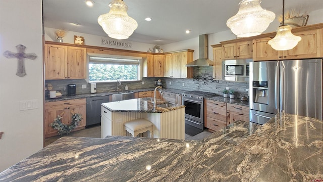 kitchen featuring wall chimney exhaust hood, stainless steel appliances, a kitchen island with sink, sink, and pendant lighting