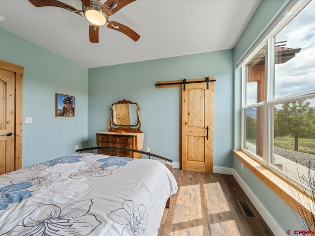 bedroom featuring ceiling fan, a barn door, and wood-type flooring