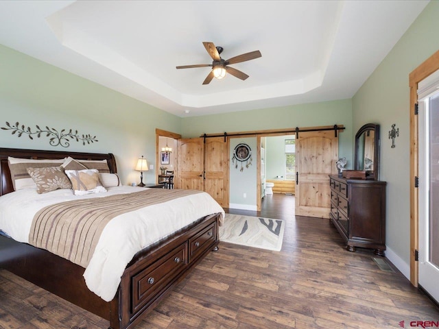 bedroom with a barn door, a tray ceiling, ceiling fan, and dark wood-type flooring