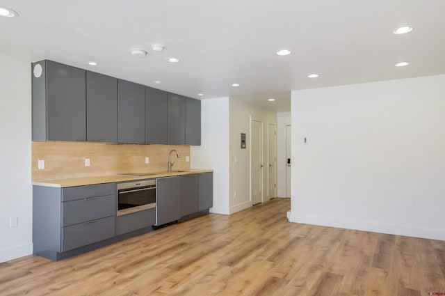 kitchen featuring sink, stainless steel appliances, tasteful backsplash, light hardwood / wood-style flooring, and gray cabinets