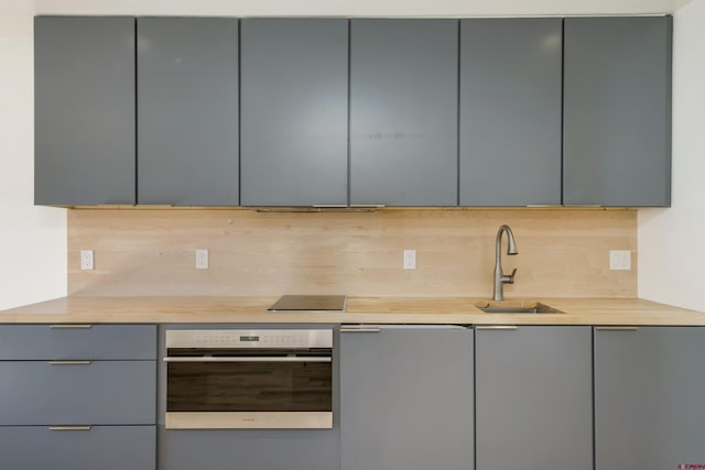 kitchen featuring gray cabinetry, stainless steel oven, sink, and tasteful backsplash