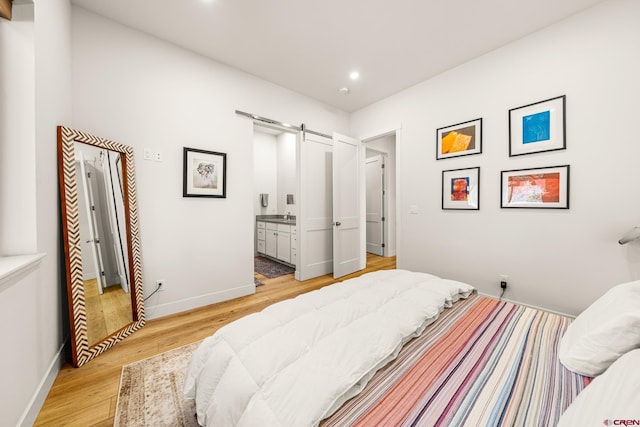 bedroom with light wood-type flooring, a barn door, and ensuite bath