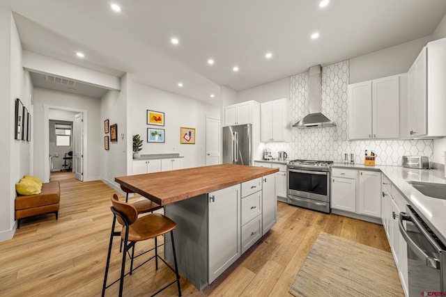 kitchen with stainless steel appliances, wall chimney range hood, white cabinets, a center island, and a breakfast bar area