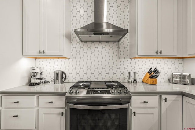 kitchen with stainless steel range with gas cooktop, white cabinets, wall chimney range hood, and tasteful backsplash