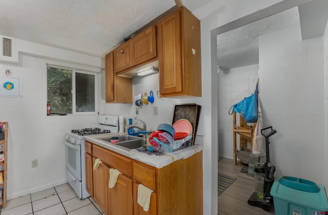 kitchen featuring white range with gas cooktop, sink, light tile patterned flooring, and a textured ceiling