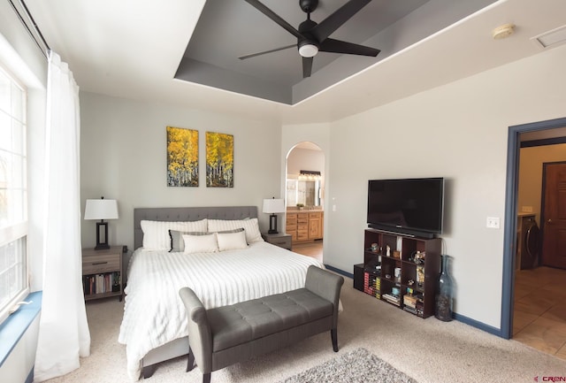 bedroom featuring connected bathroom, a tray ceiling, ceiling fan, and light colored carpet