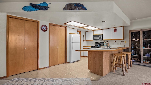 kitchen featuring kitchen peninsula, a kitchen breakfast bar, black appliances, white cabinets, and light tile patterned flooring