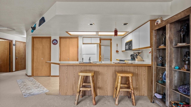 kitchen featuring kitchen peninsula, a kitchen bar, white fridge, and white cabinetry