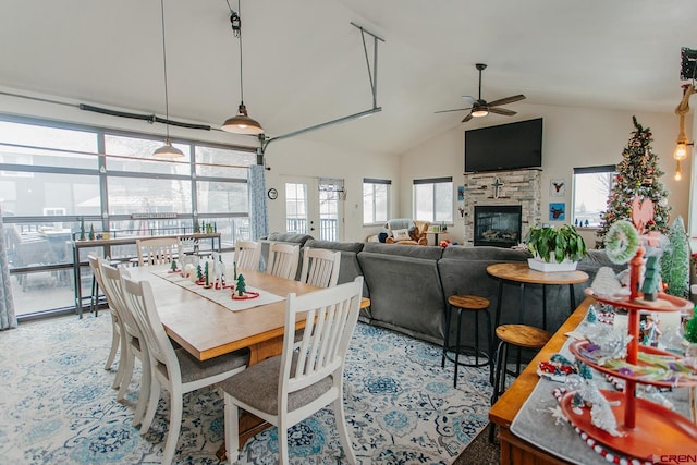 dining area with ceiling fan, a stone fireplace, and vaulted ceiling