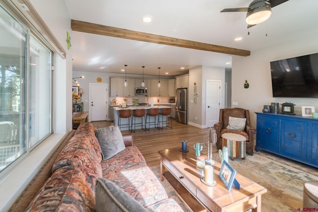 living room with beam ceiling, ceiling fan, a healthy amount of sunlight, and light wood-type flooring