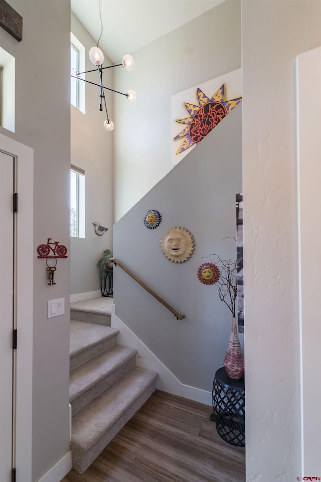 staircase with a towering ceiling, hardwood / wood-style flooring, plenty of natural light, and a notable chandelier