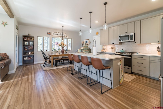 kitchen with sink, light wood-type flooring, stainless steel appliances, and a kitchen island with sink