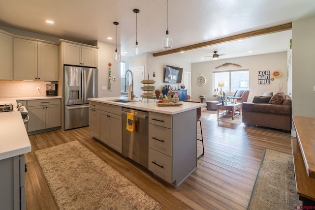 kitchen with a center island with sink, sink, ceiling fan, appliances with stainless steel finishes, and beam ceiling