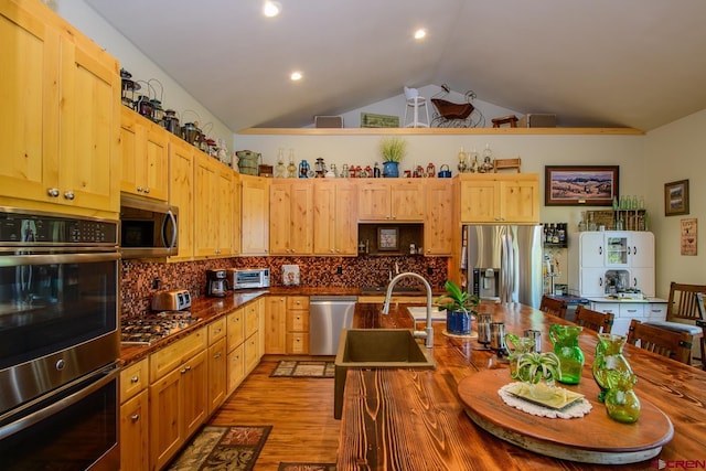 kitchen with lofted ceiling, backsplash, sink, light brown cabinetry, and stainless steel appliances