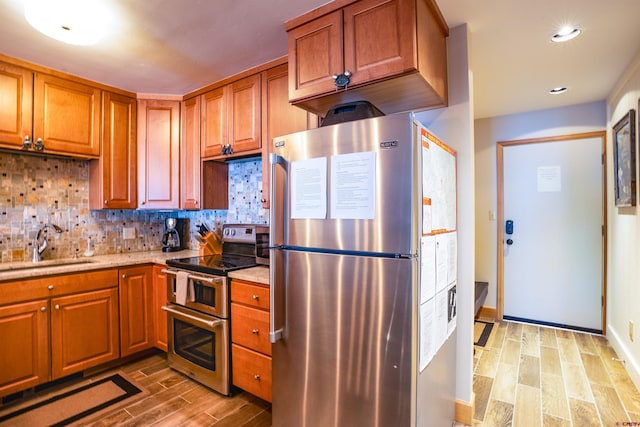 kitchen with decorative backsplash, light wood-type flooring, sink, and appliances with stainless steel finishes