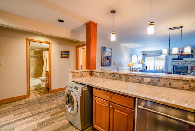 kitchen with light stone counters, stainless steel dishwasher, pendant lighting, washer / dryer, and a fireplace