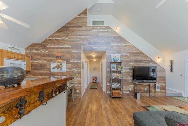 living room with ceiling fan, wood walls, light hardwood / wood-style flooring, and vaulted ceiling