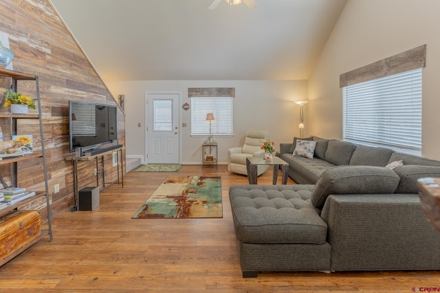 living room featuring lofted ceiling, light hardwood / wood-style floors, ceiling fan, and wooden walls