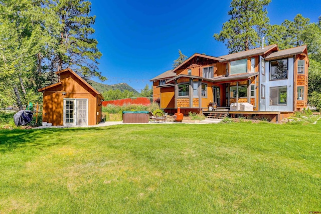 rear view of house featuring a mountain view, a hot tub, an outdoor structure, and a lawn