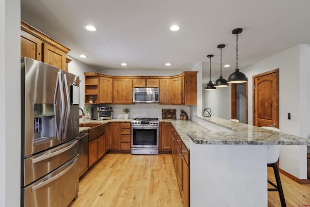 kitchen featuring kitchen peninsula, a kitchen breakfast bar, stainless steel appliances, light hardwood / wood-style floors, and hanging light fixtures