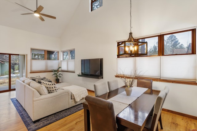 dining space featuring high vaulted ceiling, wood-type flooring, and ceiling fan with notable chandelier