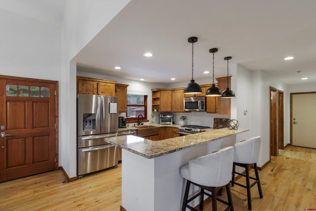 kitchen featuring light stone countertops, kitchen peninsula, pendant lighting, appliances with stainless steel finishes, and light wood-type flooring