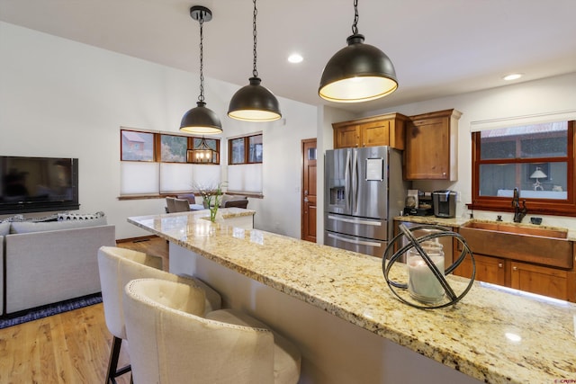 kitchen with light stone counters, sink, stainless steel fridge with ice dispenser, hanging light fixtures, and a breakfast bar area