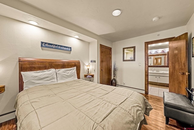 bedroom with a closet, wood-type flooring, a baseboard heating unit, and ensuite bath